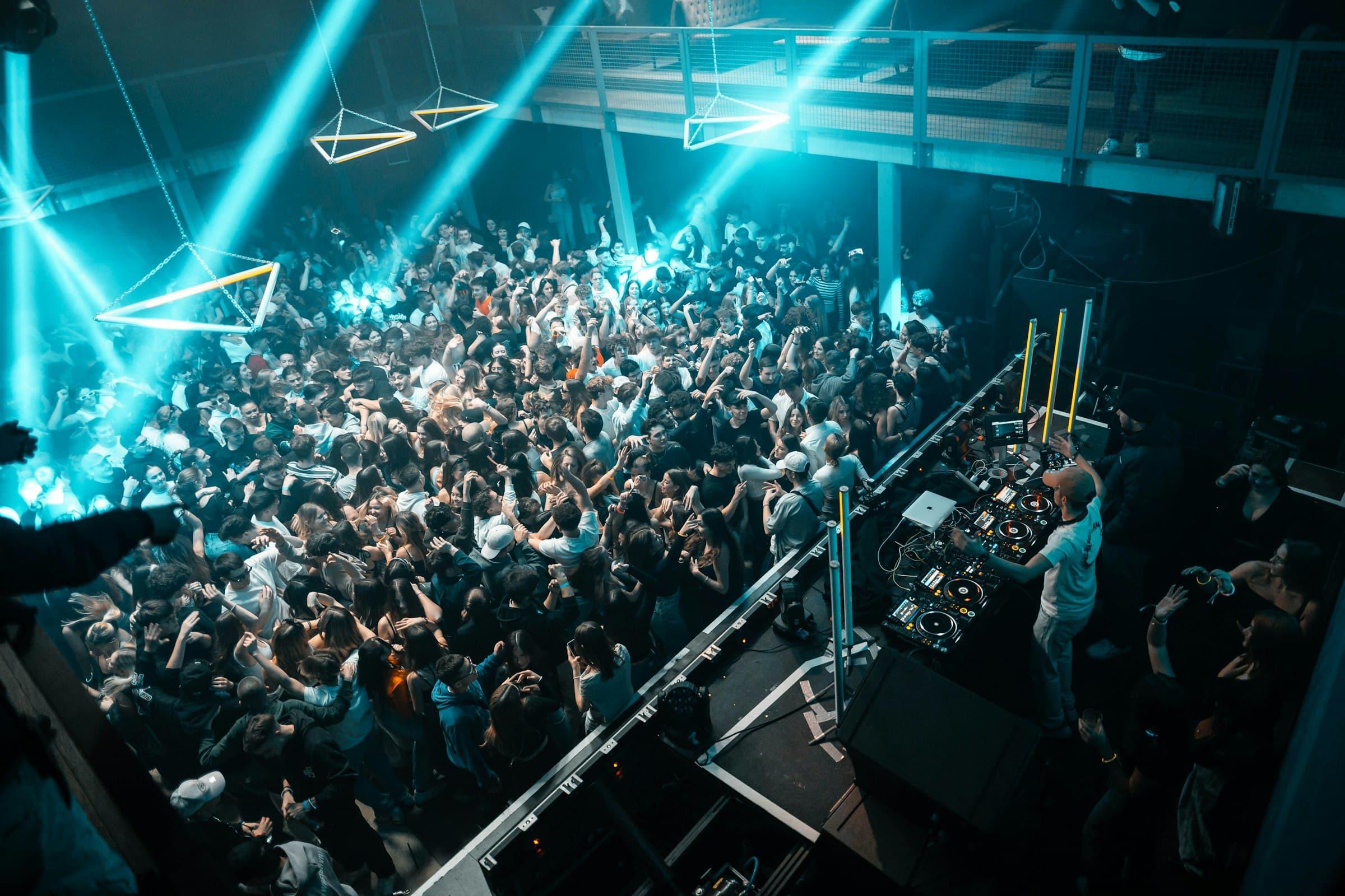 Público bailando en un club visto desde arriba, con luces azules y el DJ a la derecha